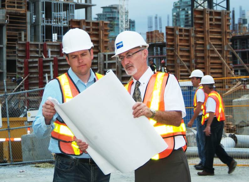 A group of men wearing safety vests and helmets looking at a blueprint

Description automatically generated